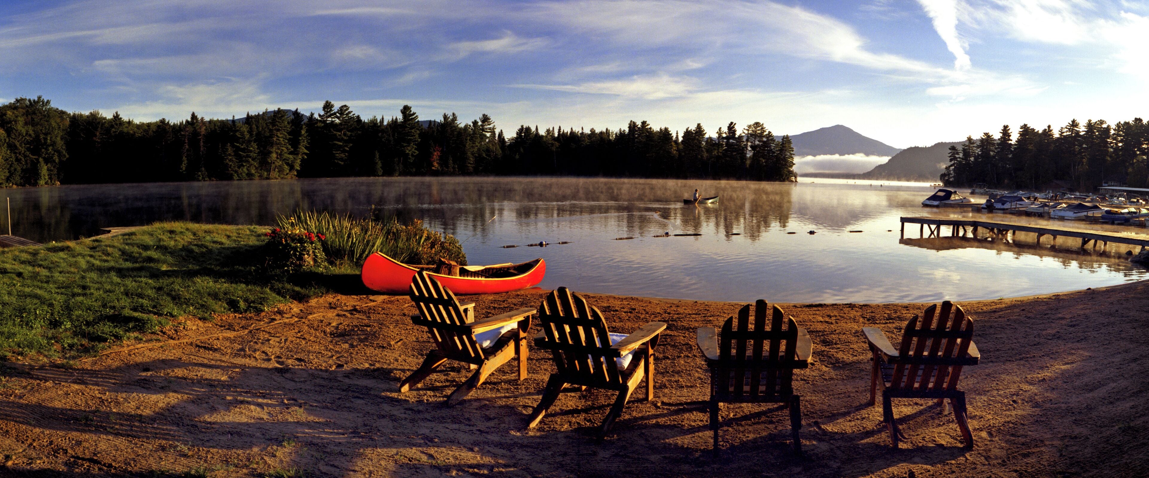 A lakeside setting with canoes, chairs, and a dock.