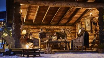 A log cabin with a fire pit, wooden furniture, and a Christmas tree.