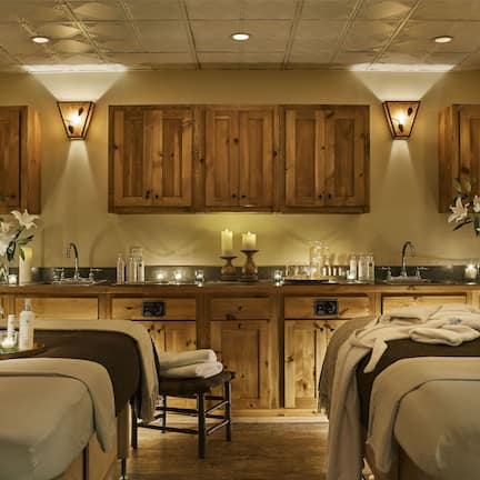 A spa room with wooden cabinets, a sink, and two beds with towels.