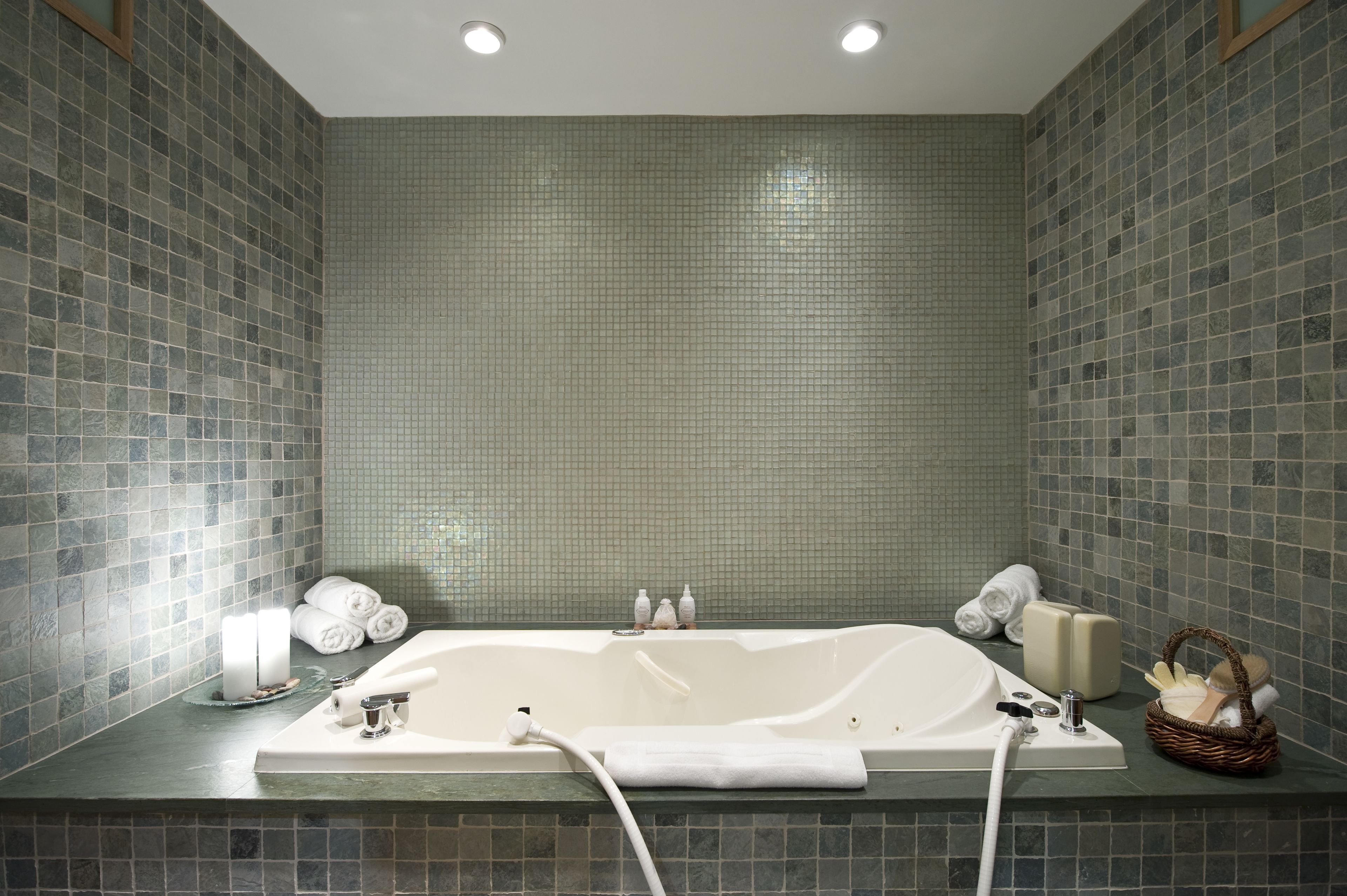 A bathroom with a large bathtub, tiled walls, and various toiletries on the counter.