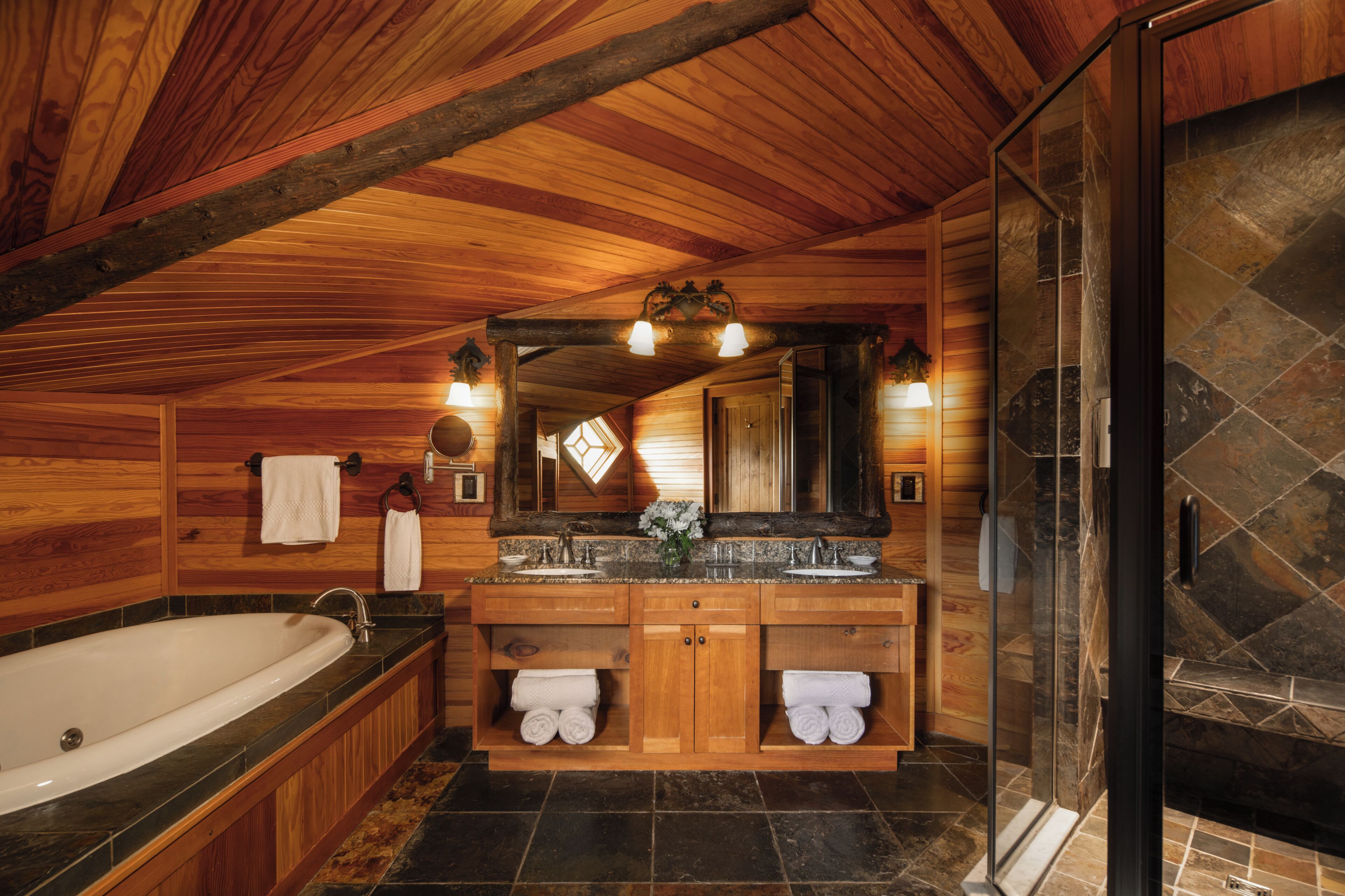Ein Badezimmer einer Holzhütte mit Badewanne, doppelter Waschtisch und einer Duschkabine aus Glas.