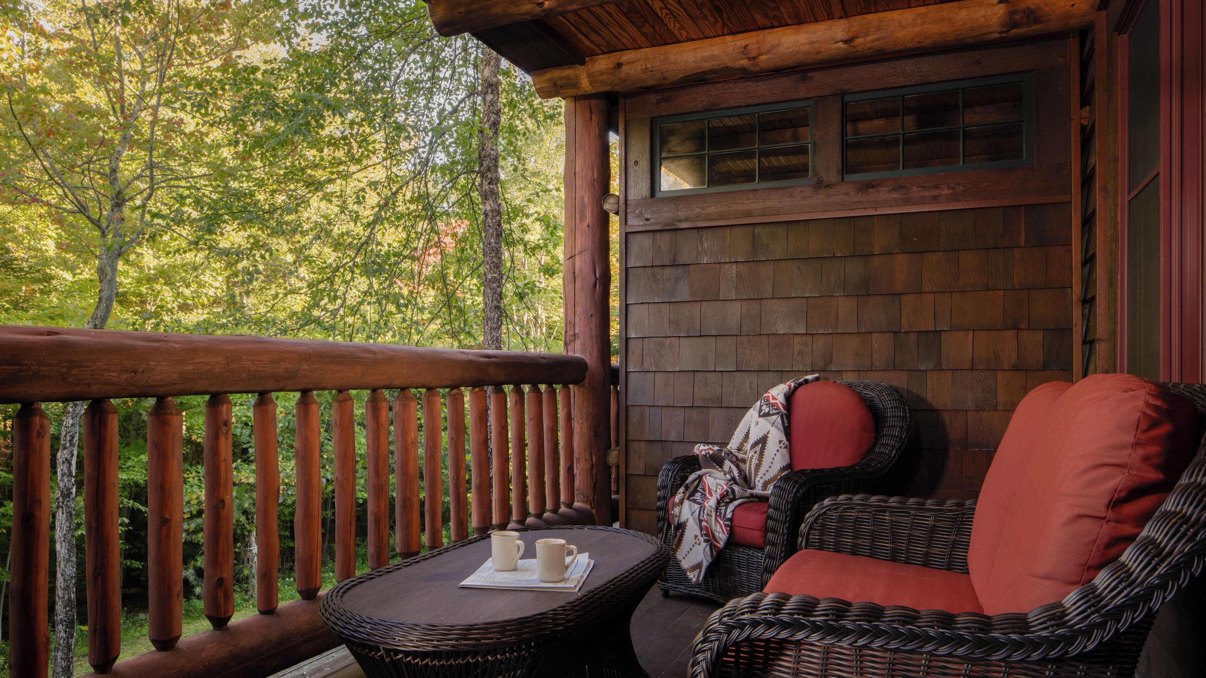 A wooden deck with wicker furniture and a table, surrounded by trees.