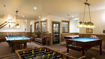 A room with a pool table, a foosball table, and a billiards table. There are wooden walls and a staircase leading to another level.