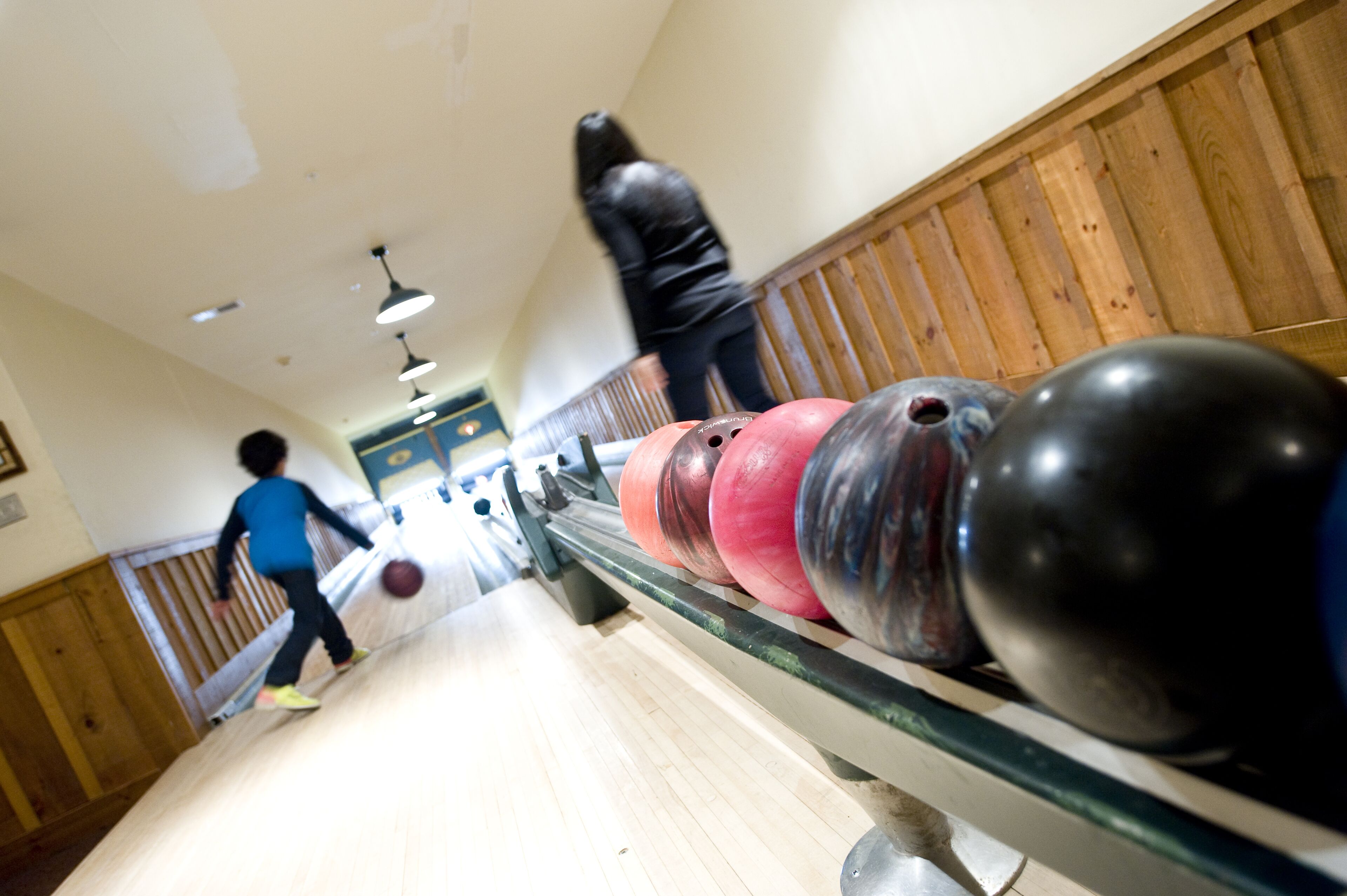 A bowling alley with wooden paneling and a person bowling.