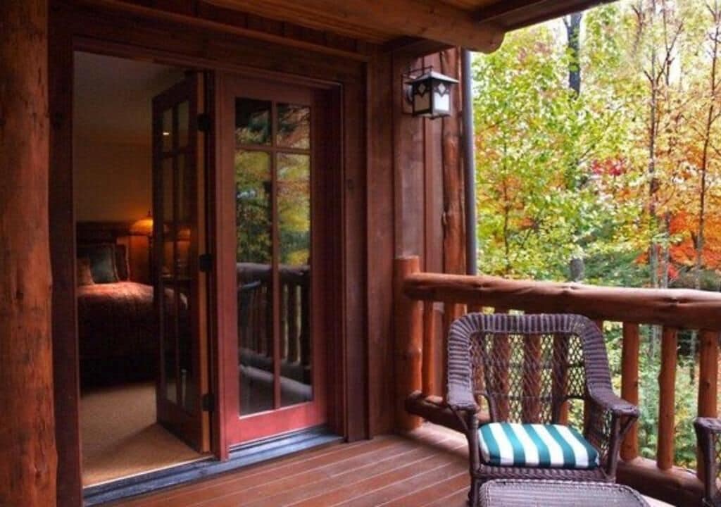 A wooden deck with a wicker chair and a sliding glass door leading to a room.