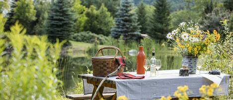 A picnic setup with a table, basket, wine bottle, and flowers in a natural setting.