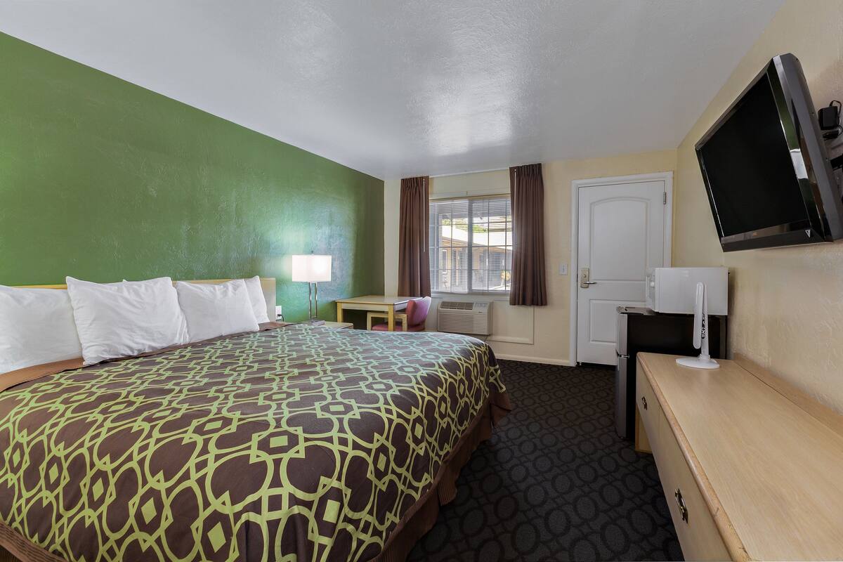 A hotel room with a large bed, a desk, a TV, and a window with curtains.