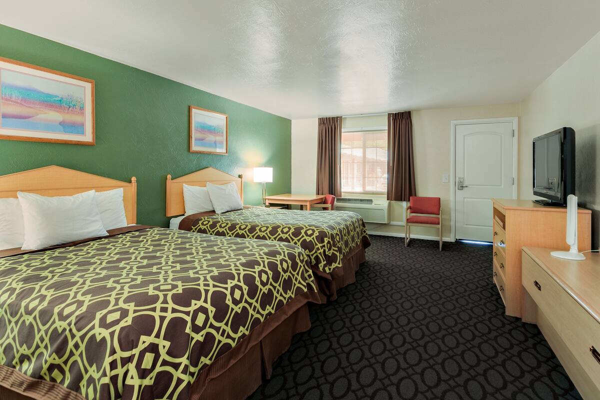 A hotel room with two beds, a desk, a chair, a TV, and a window with curtains.