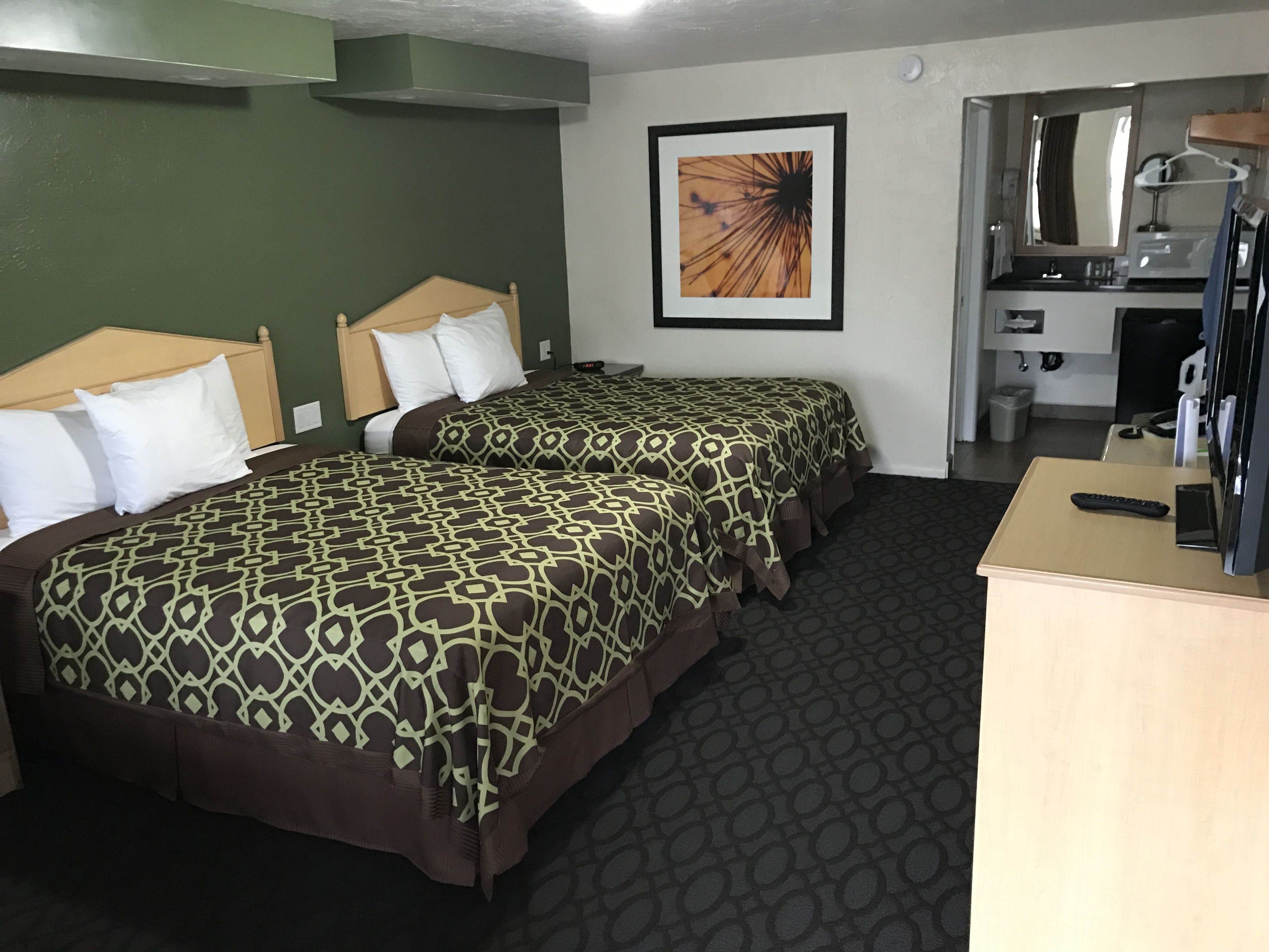 Une chambre d’hôtel avec deux lits, un bureau, une chaise, une télévision et une salle de bain visible à travers une porte ouverte.