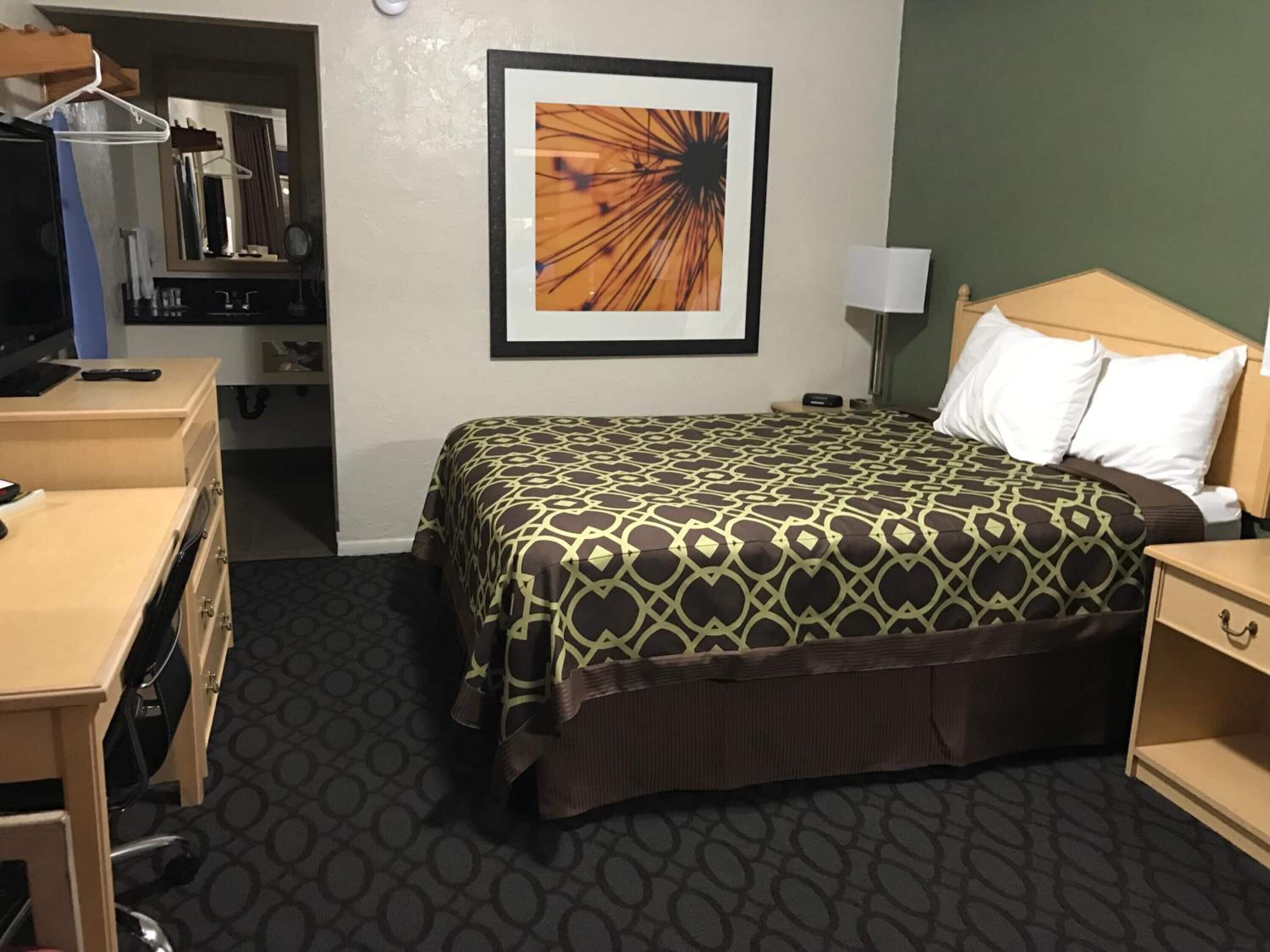 Une chambre d’hôtel avec un lit, un bureau, une chaise, une armoire et un tableau encadré au mur.