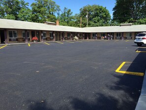 A motel with a large parking lot, multiple rooms, and a central area with benches.