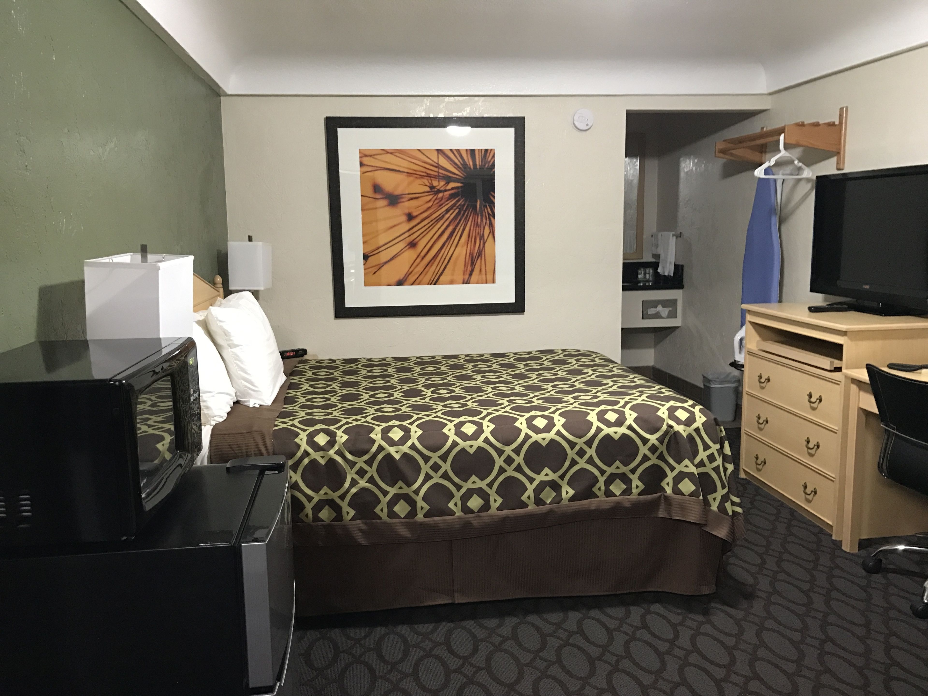 A hotel room with a bed, a desk, a television, a dresser, and a framed picture on the wall.