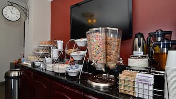Un bufé de desayuno con diversos alimentos, un reloj y un televisor en la pared.