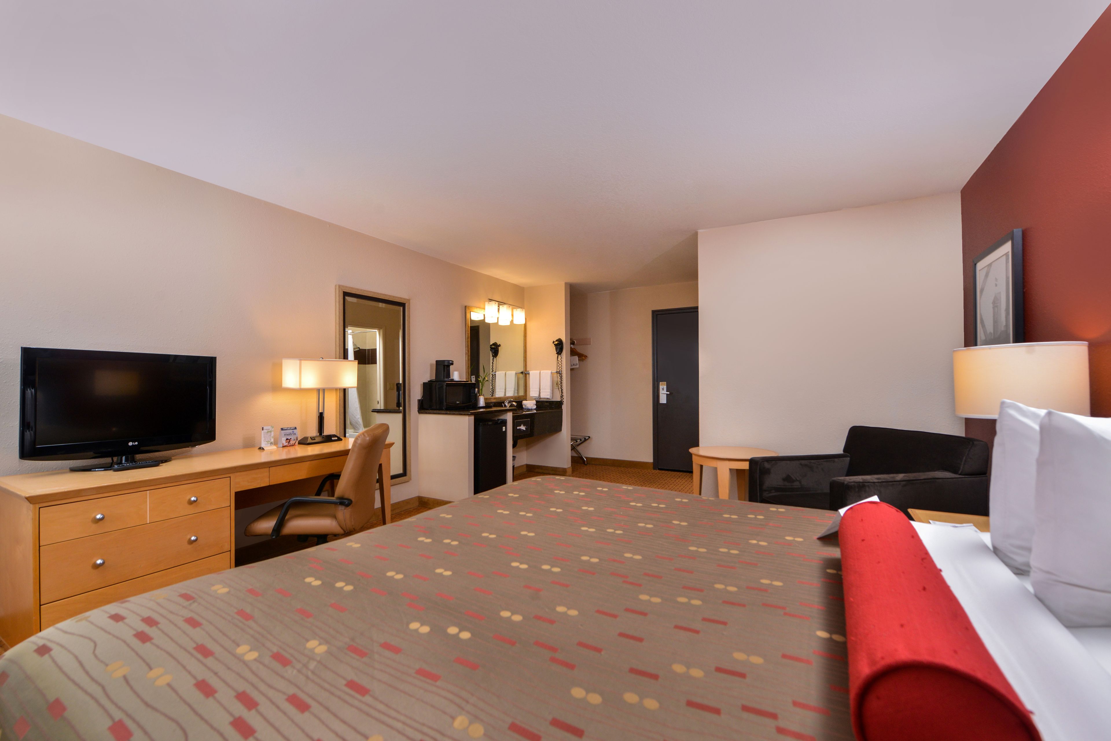 A hotel room with a bed, a desk, a television, a chair, and a desk lamp.