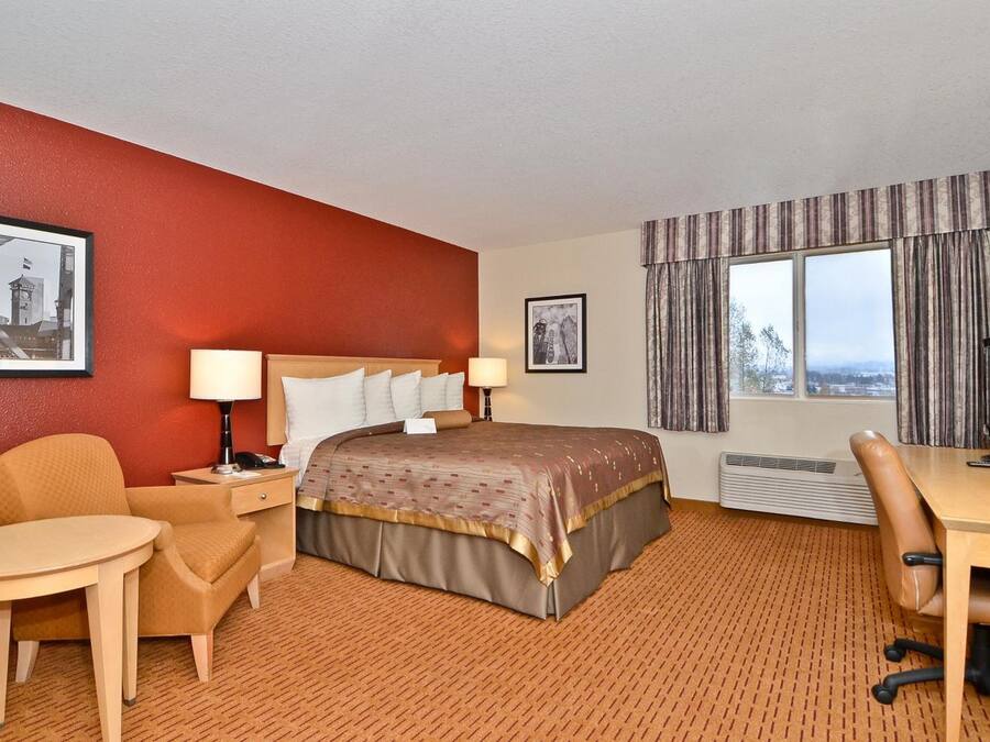 Une chambre d’hôtel comprenant un lit, deux tables de chevet, un bureau, une chaise, une petite table et une fenêtre avec des rideaux.