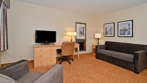 A hotel room with a TV, a desk, a chair, a sofa, and two framed pictures on the wall.
