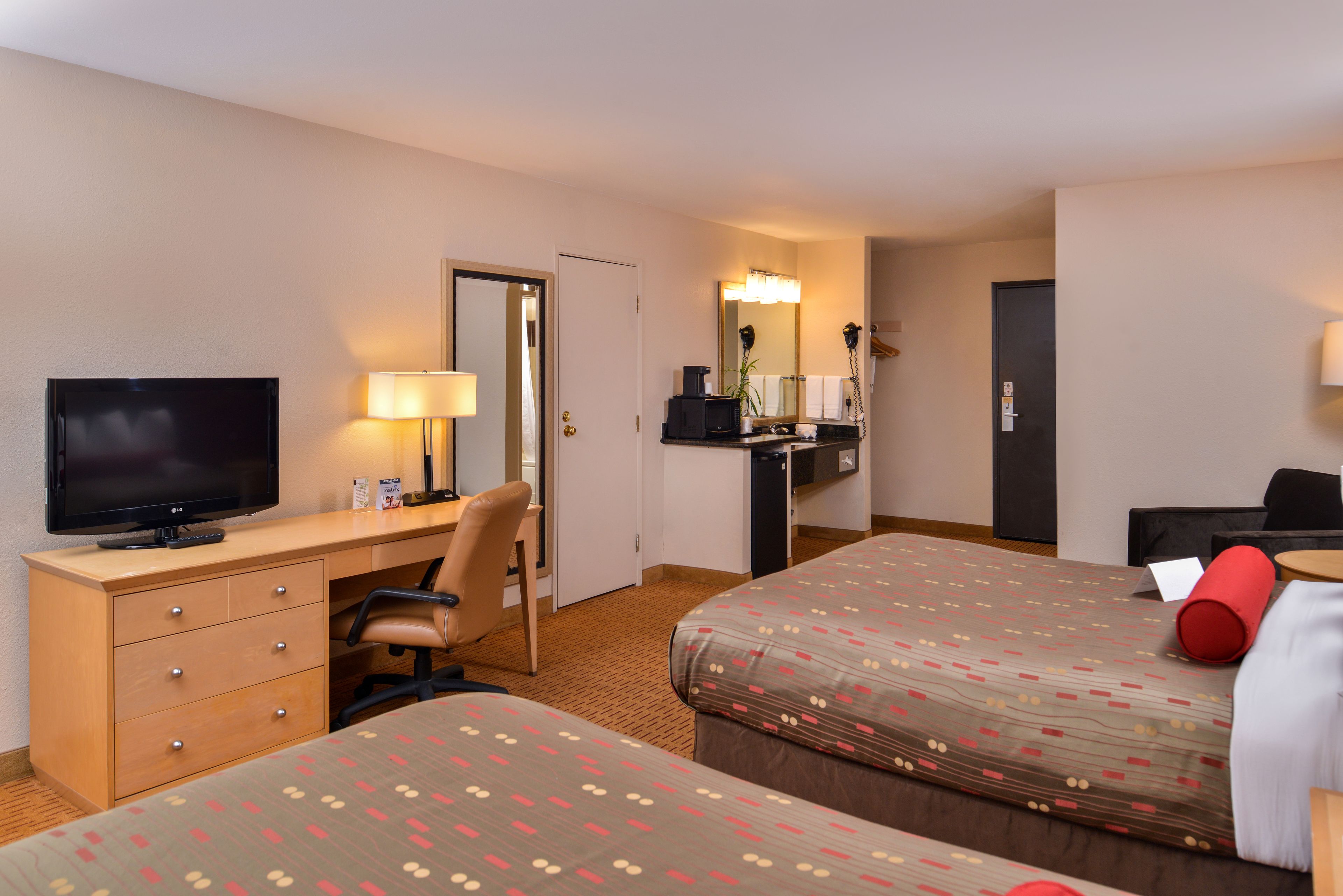 A hotel room with two beds, a desk with a TV, a chair, a desk lamp, a mirror, and a phone.