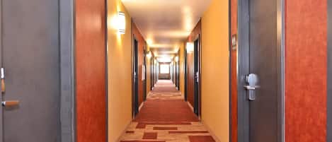 Ein Hotelgang mit Teppichboden, Türen auf beiden Seiten und Wandleuchten.