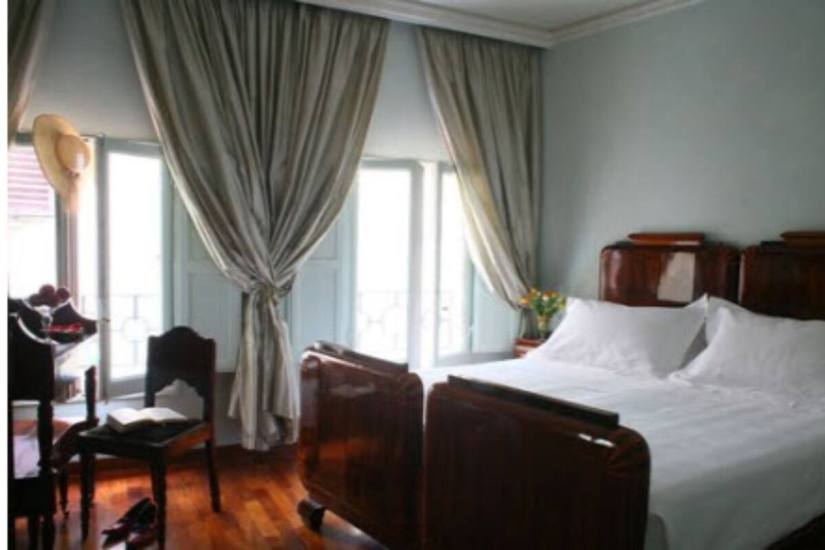 Ein Hotelzimmer mit einem großen Bett, einem Holzkopfende, einem Schreibtisch mit Stuhl und einem Fenster mit Vorhängen.