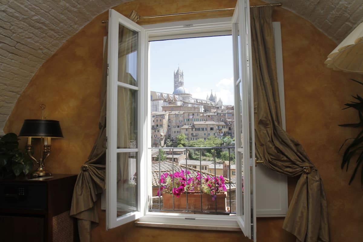 Ein offenes Fenster mit Blick auf eine Stadtlandschaft, eine Lampe und ein Topfpflanze auf einem Holztisch.
