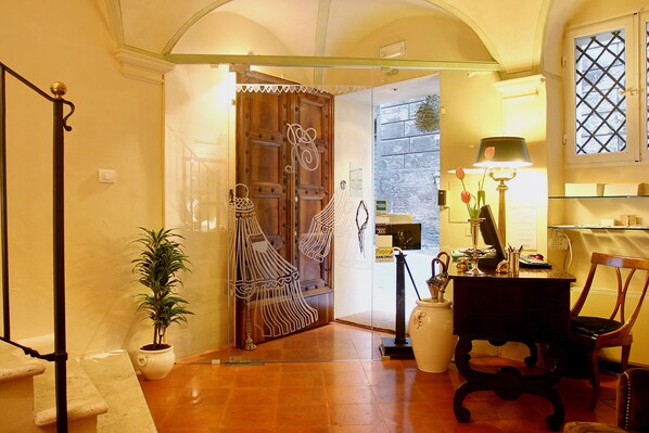 A room with a wooden door, a potted plant, a desk with a lamp, and a chair.