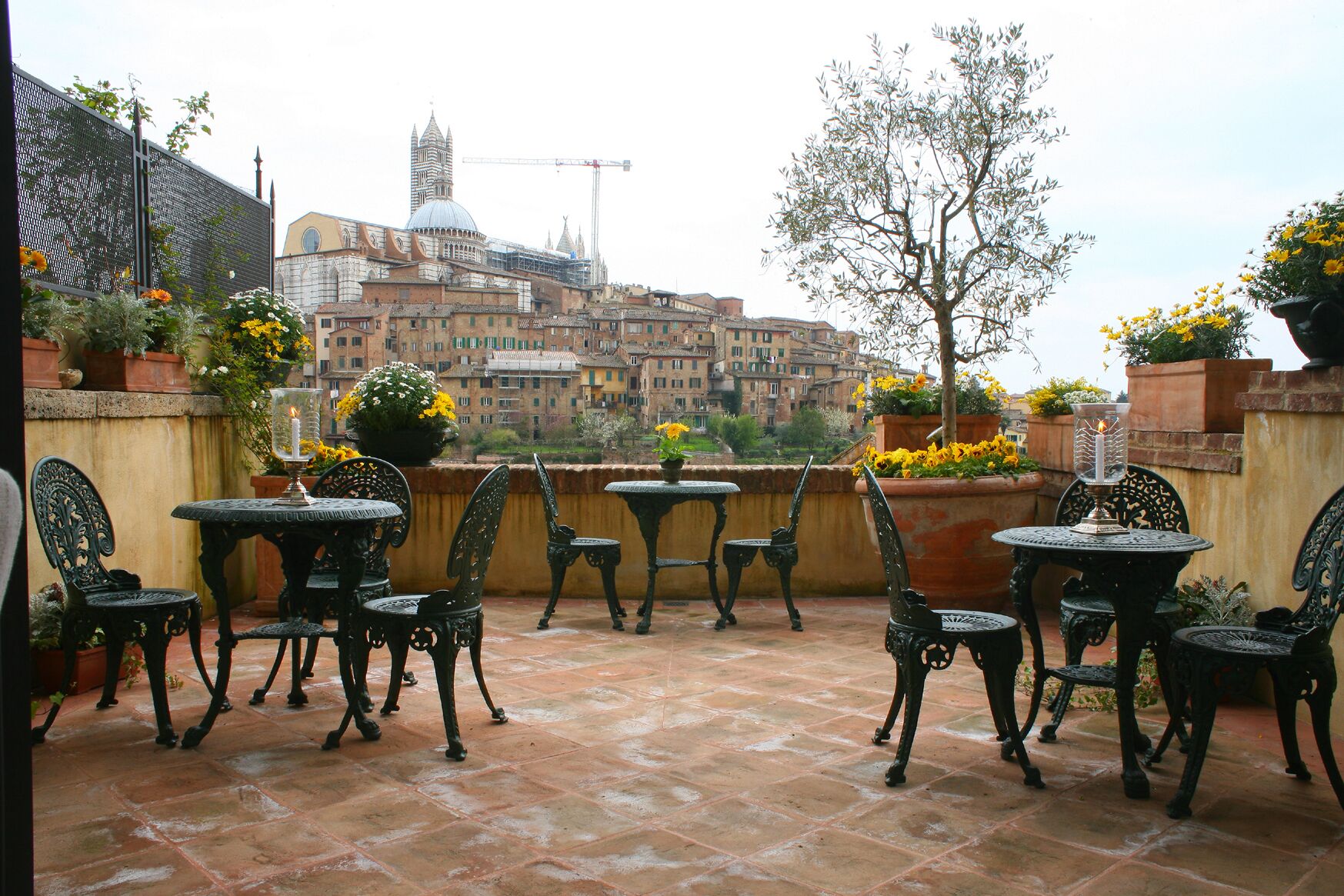 An outdoor patio with tables and chairs, potted plants, and a view of historic buildings in the background.