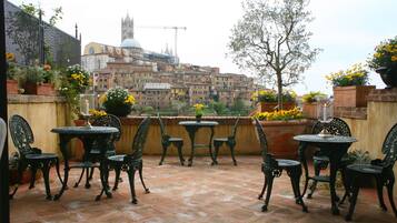 An outdoor patio with tables and chairs, potted plants, and a view of historic buildings in the background.