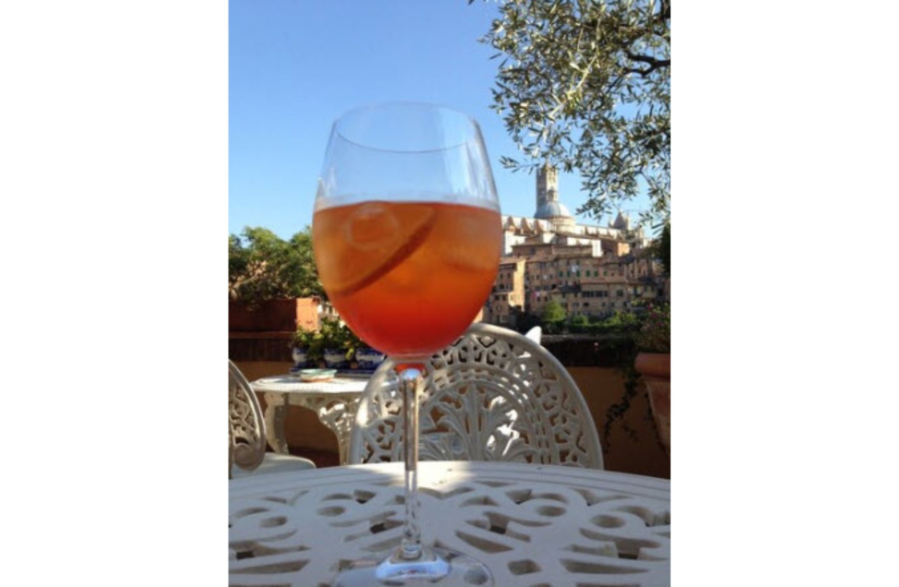 Um copo de vinho tinto sobre uma mesa ao ar livre, com vista para um edifício histórico ao fundo.