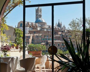 A view from a balcony with a table and chairs, overlooking a historic town with distinctive architecture, including a prominent tower and a dome.