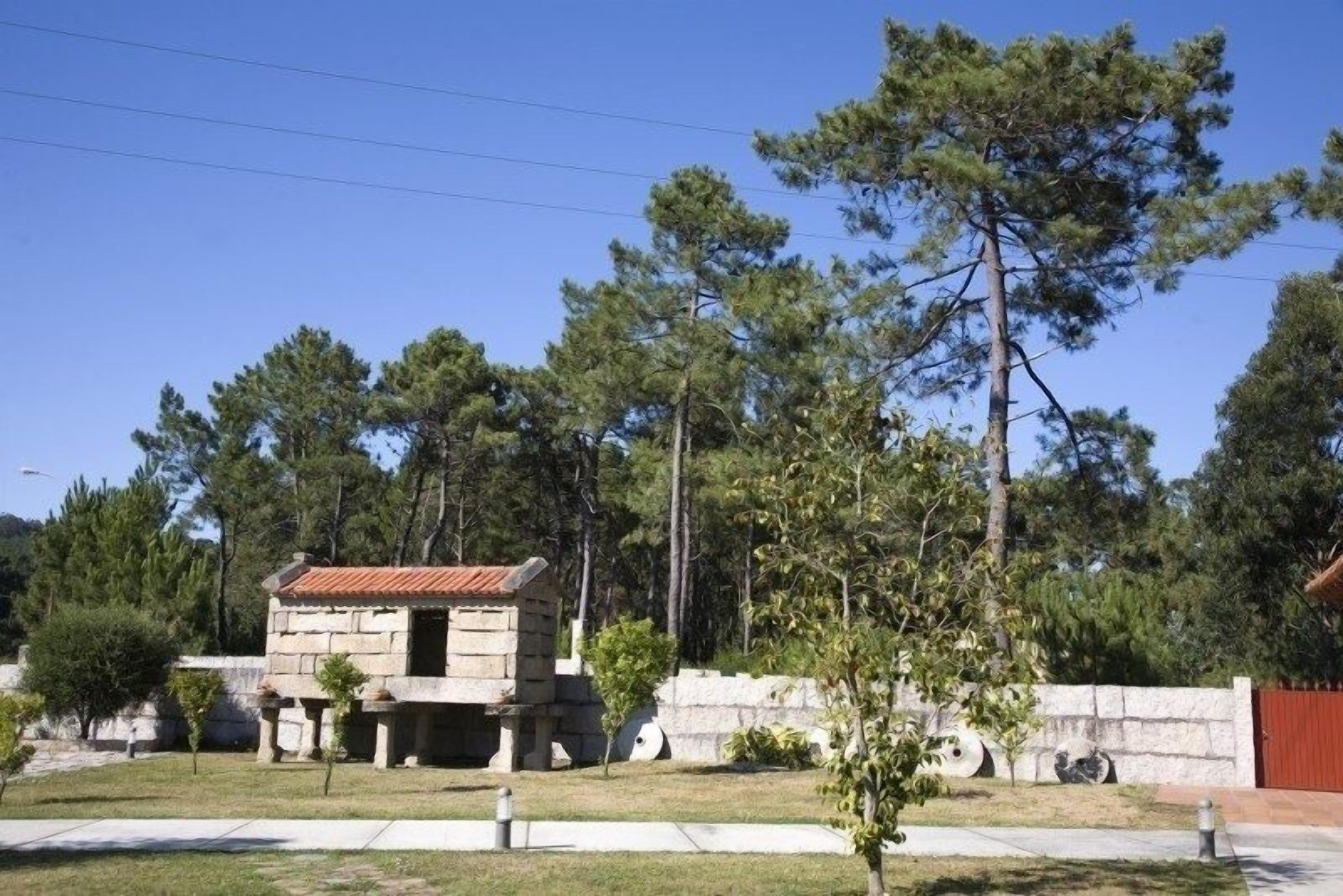 A stone building with a tiled roof, surrounded by trees and a stone wall.