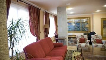 Una sala de estar con un sofá rojo, sillones estampados, una mesa de centro de vidrio y un cuadro grande en la pared.