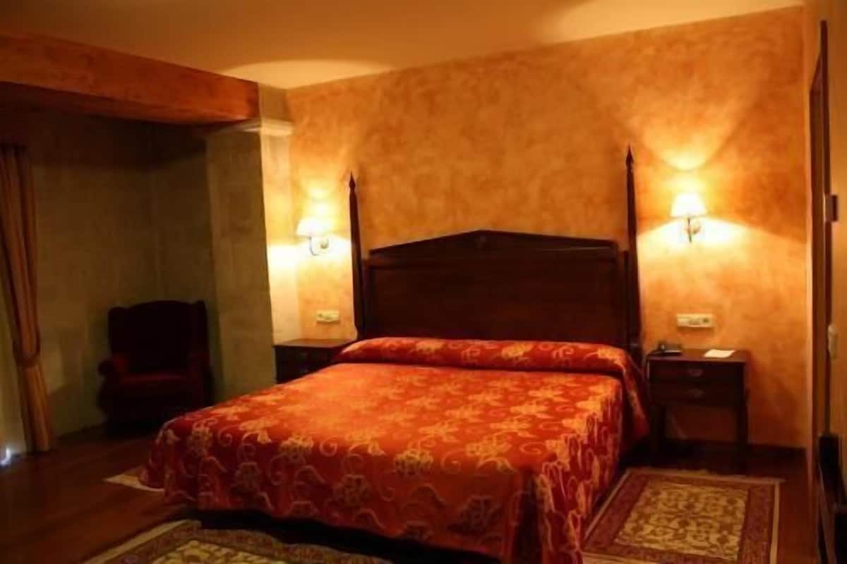 A hotel room with a large bed, two bedside tables, a nightstand, and a chair.