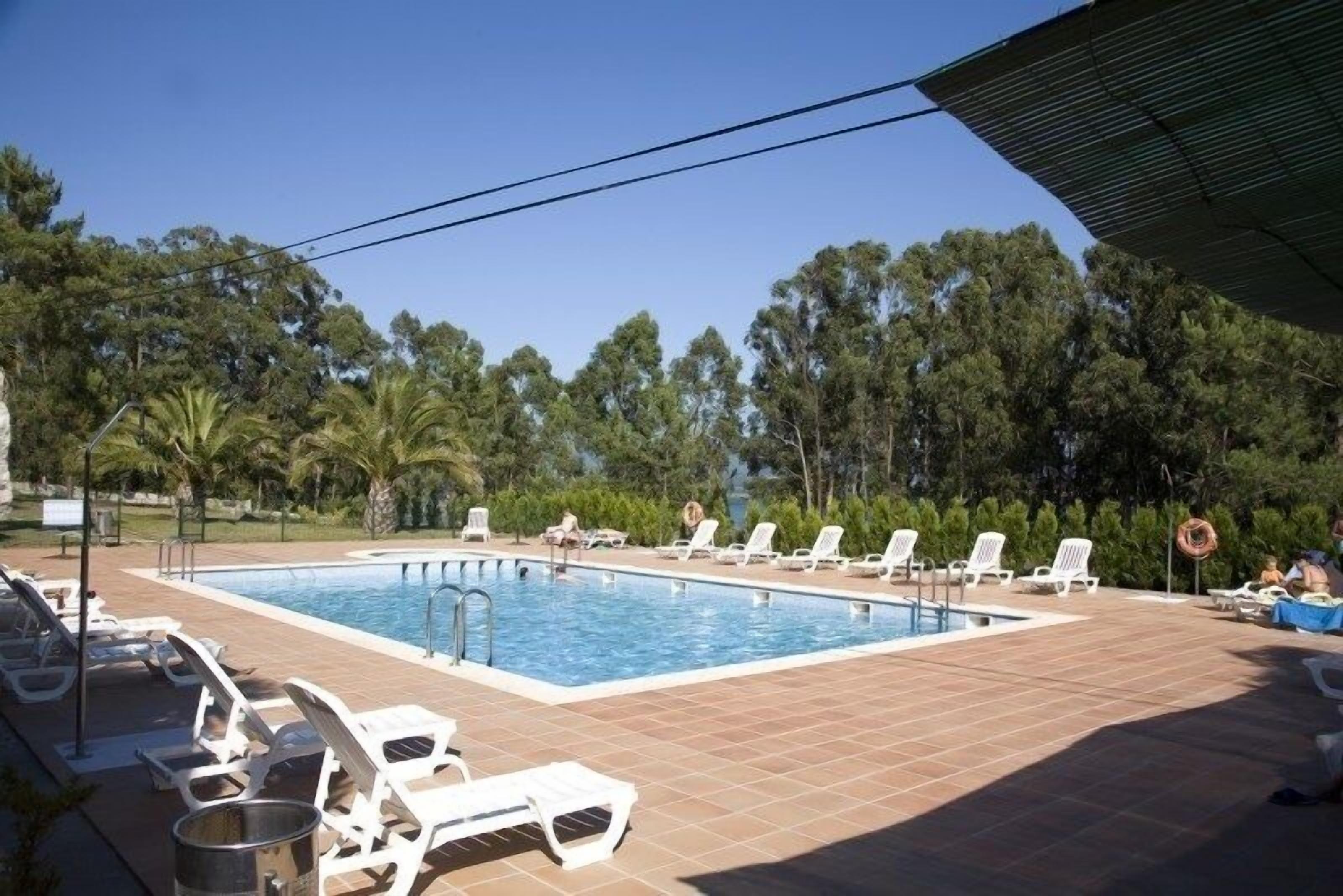 A swimming pool with sun loungers and a tiled deck, surrounded by trees.