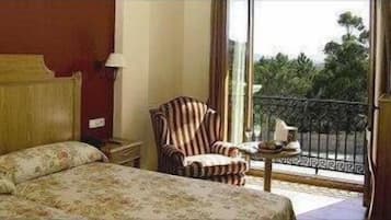 A hotel room with a bed, a chair, a nightstand, and a window with a view of greenery.