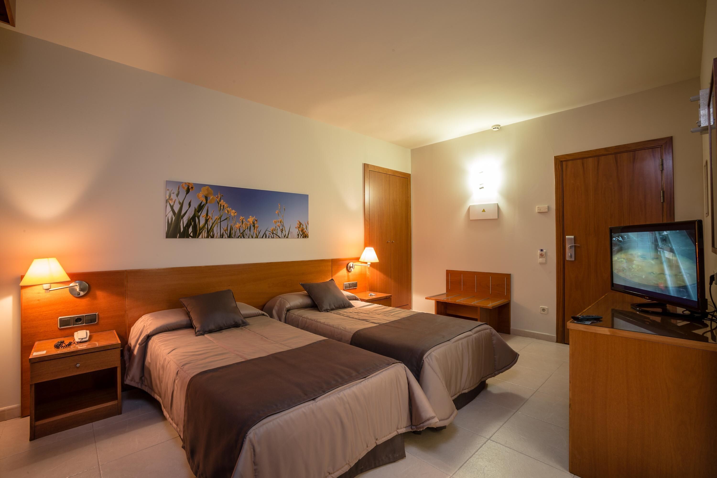 A hotel room with two beds, a television, a painting, and a desk.
