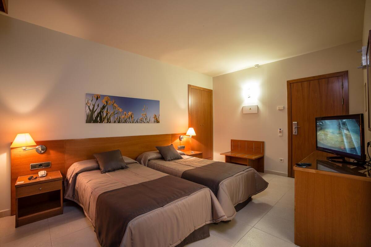 A hotel room with two beds, a television, a painting, and a desk.