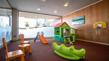 Zona de juegos infantiles con una casita, un tobogán y un aro de baloncesto.