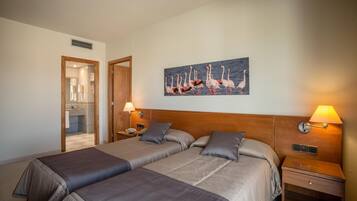 A hotel room with two beds, a wooden headboard, a nightstand with a lamp, and a painting of flamingos on the wall.