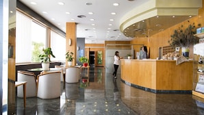 A modern hotel lobby with a reception desk, seating area, and large windows. - Hotel Rull (Deltebre)