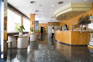 Un moderno vestíbulo de hotel con una recepción, zona de estar y grandes ventanales.