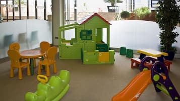 Un área de juegos infantiles con una casita, sillas, una mesa y un tobogán.