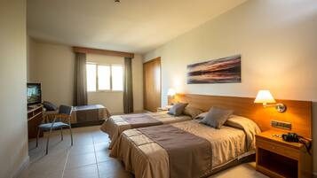 Habitación de hotel con dos camas, un escritorio con silla, un televisor y un cuadro en la pared.