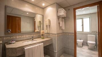 Un baño con lavabo, espejo, toallero y dos inodoros.