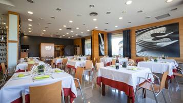 A restaurant with multiple tables set for dining, featuring a modern interior with recessed lighting and a large abstract painting on the wall.