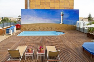 Un área de piscina en la azotea con cubierta de madera, sillones de descanso y un gran mural de un faro.