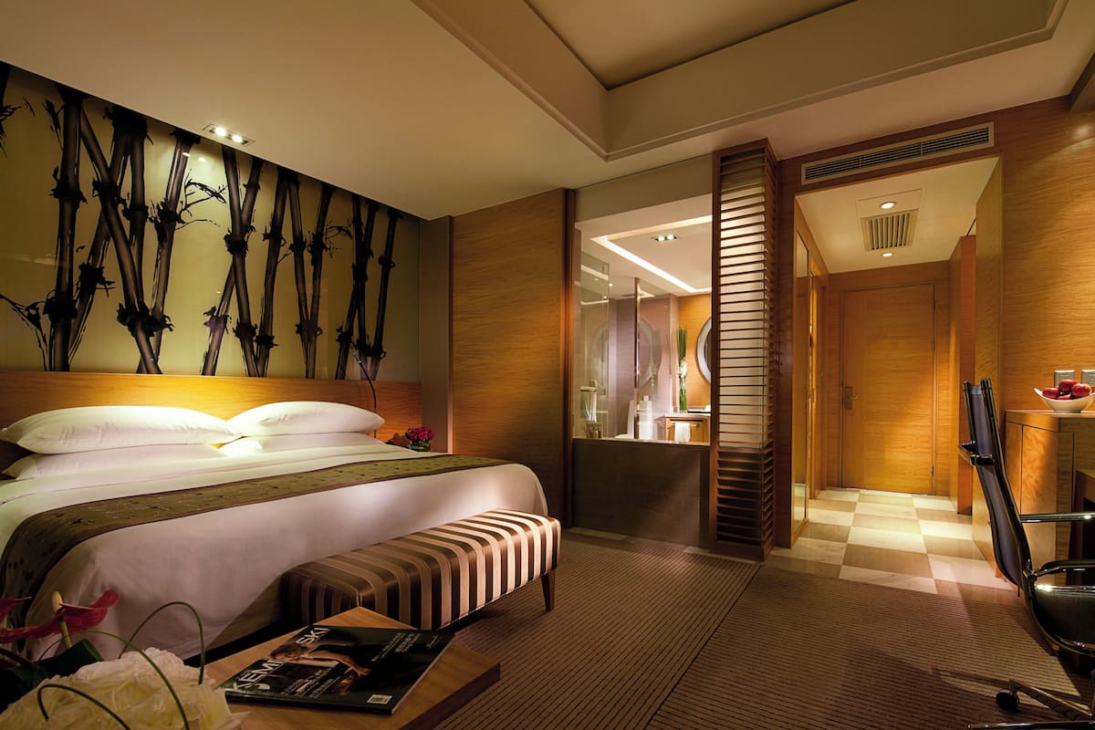 Ein Hotelzimmer mit einem großen Bett, einem Nachttisch mit einer Zeitschrift, einer Bank und einer Wand mit Bambusmuster.