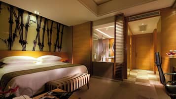 Une chambre d’hôtel avec un grand lit, une table de chevet avec un magazine, un banc et un mur décoré de motifs en bambou.