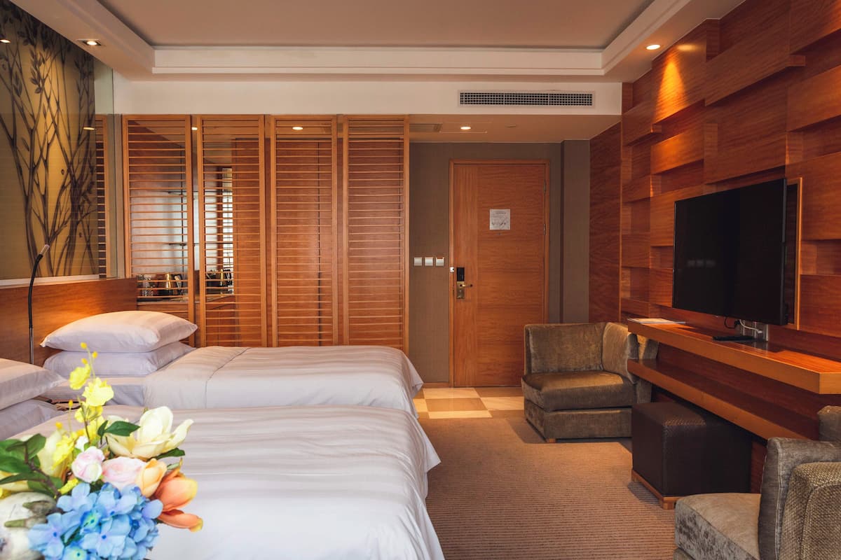 Ein Hotelzimmer mit zwei Betten, einem Fernseher, einer Sitzecke und einer Wandverkleidung aus Holz.
