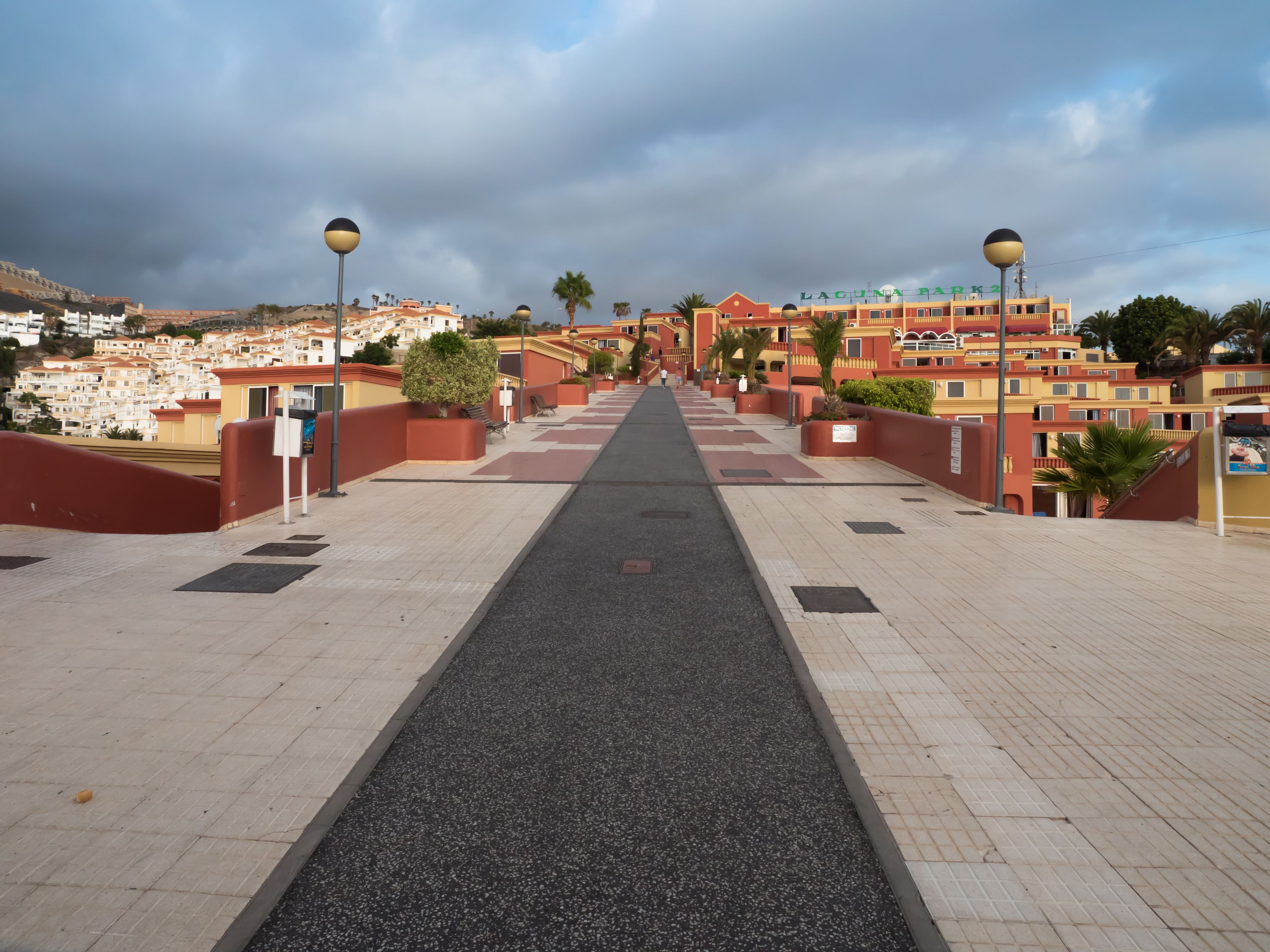 Ein Weg führt zu einem Gebäude mit Balkonen, einem klaren Himmel und einer weiten Aussicht auf eine Stadt.