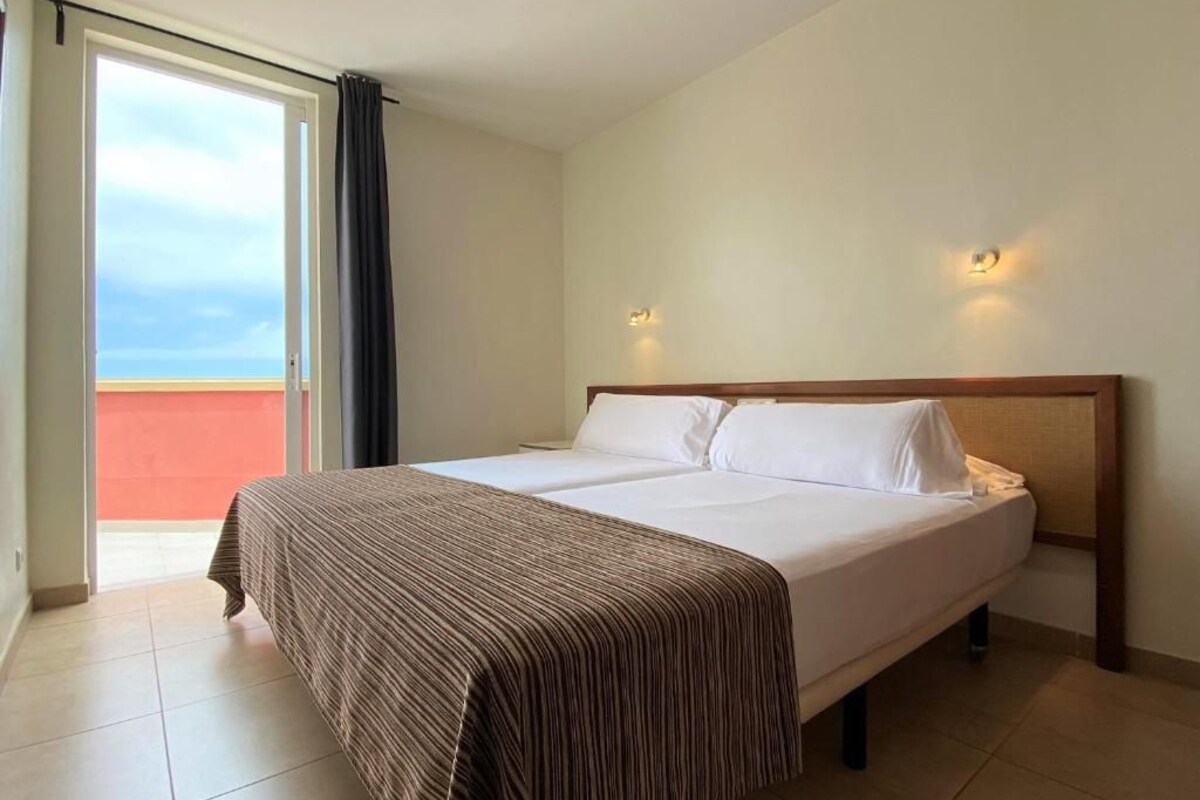 Een hotelkamer met een bed, uitzicht door een schuifdeur en twee wandlampen.